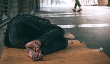 Close up feet of poor homeless man or refugee sleeping on the dirty floor on the urban street in the city.